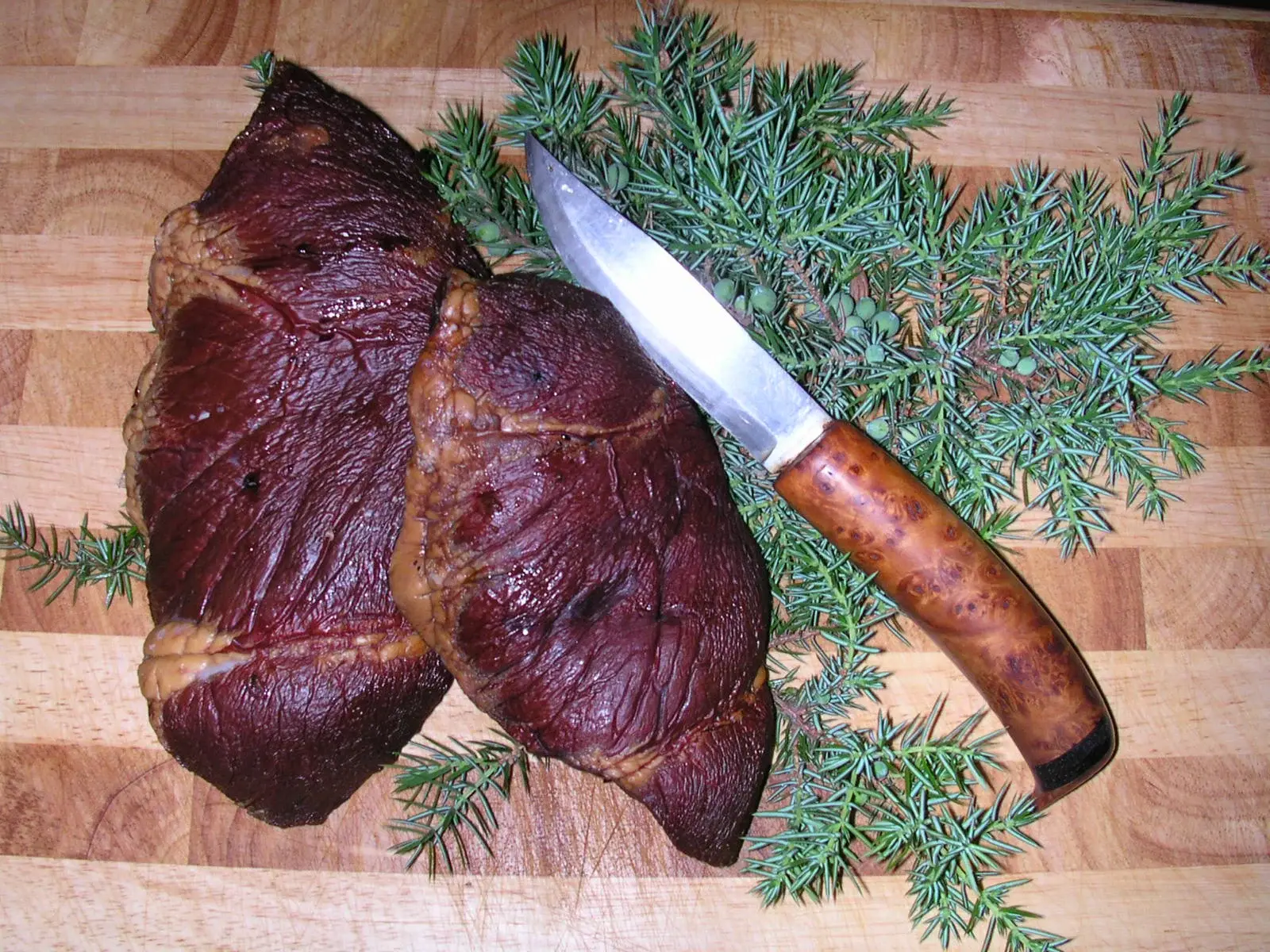 Rökt hjorthjärta på skärbräda med kniv och enris